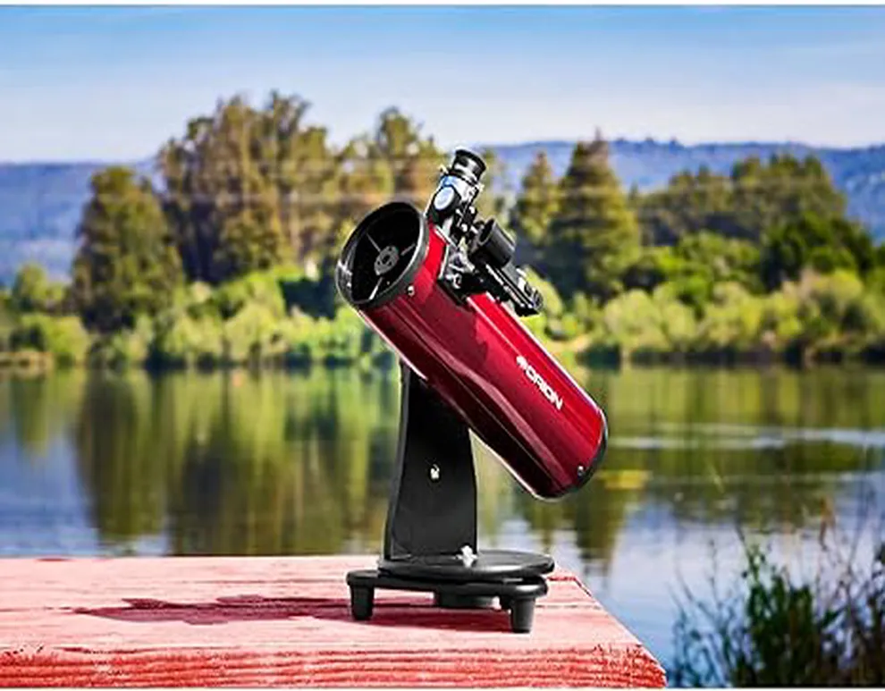 Telescopio Orion SkyScanner 100mm montado sobre una mesa al aire libre, con un paisaje natural de fondo, ideal para observaciones astronómicas en entornos naturales.